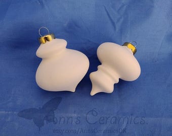 Peut inclure: Deux décorations de Noël en céramique blanche avec des capuchons en métal doré et des cintres en fil de fer. Les décorations ont des formes bulbeuses uniques. Elles sont présentées sur un fond bleu. Le nom de la boutique Etsy, "Ann's Ceramics", est visible.