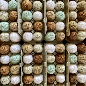 May include: A carton of crocheted eggs in various colours, including white, brown, and green. The eggs are arranged in rows and columns, creating a visually appealing pattern.