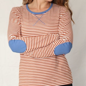 May include: A long-sleeved striped shirt with blue elbow patches. The shirt has white and orange stripes.