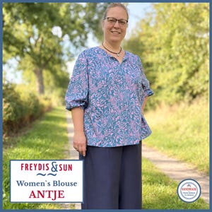 Könnte beinhalten: Eine Bluse mit blaugrünem und rosafarbenem Blumenmuster, Dreiviertelärmeln und V-Ausschnitt, kombiniert mit einer einfarbigen, dunkelblauen Hose mit weitem Bein. Die Bluse zeigt ein sich wiederholendes Muster aus stilisierten Blättern und Blüten.