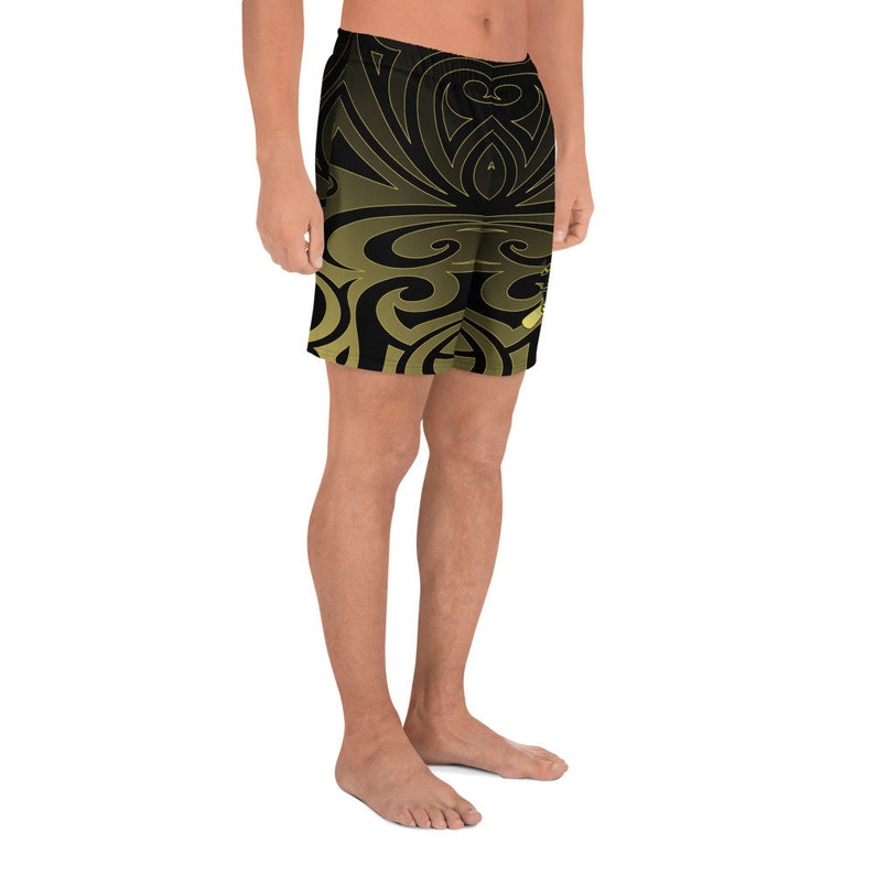 May include: Black and gold patterned shorts. The shorts feature a repeating design of swirling shapes and lines. The color gradient transitions from gold to black. The shorts are made of a lightweight material.