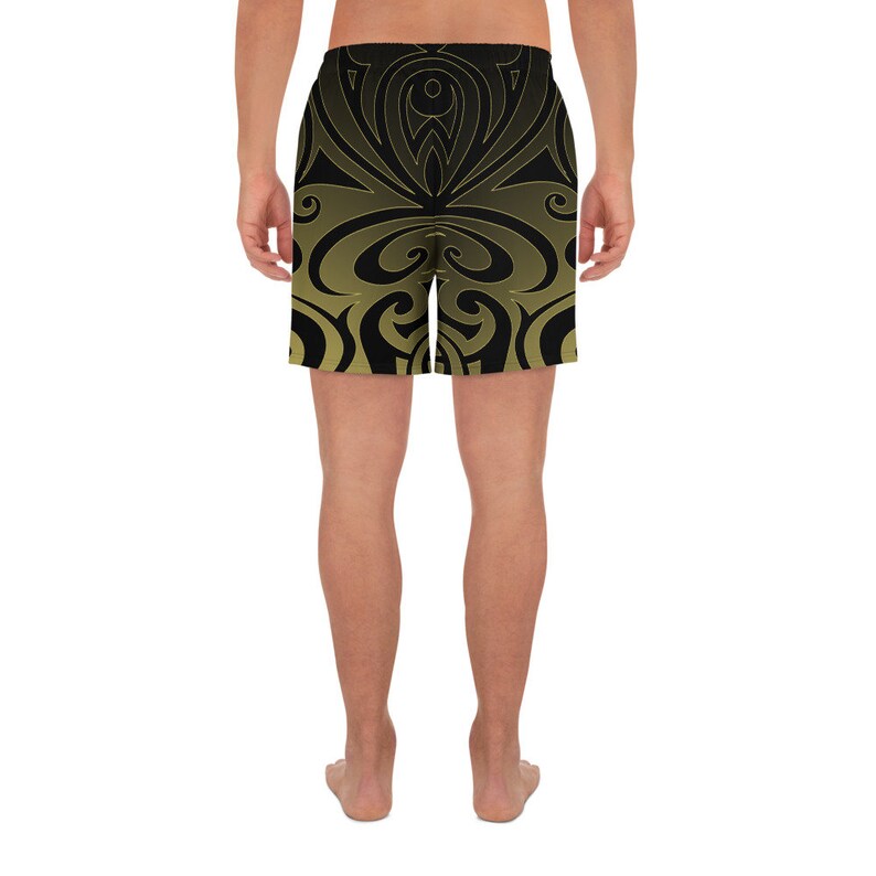 May include: Black and gold athletic shorts with a symmetrical, swirling design. The shorts have a gradient effect, transitioning from black at the top to gold at the bottom. The shorts are designed for athletic activities.