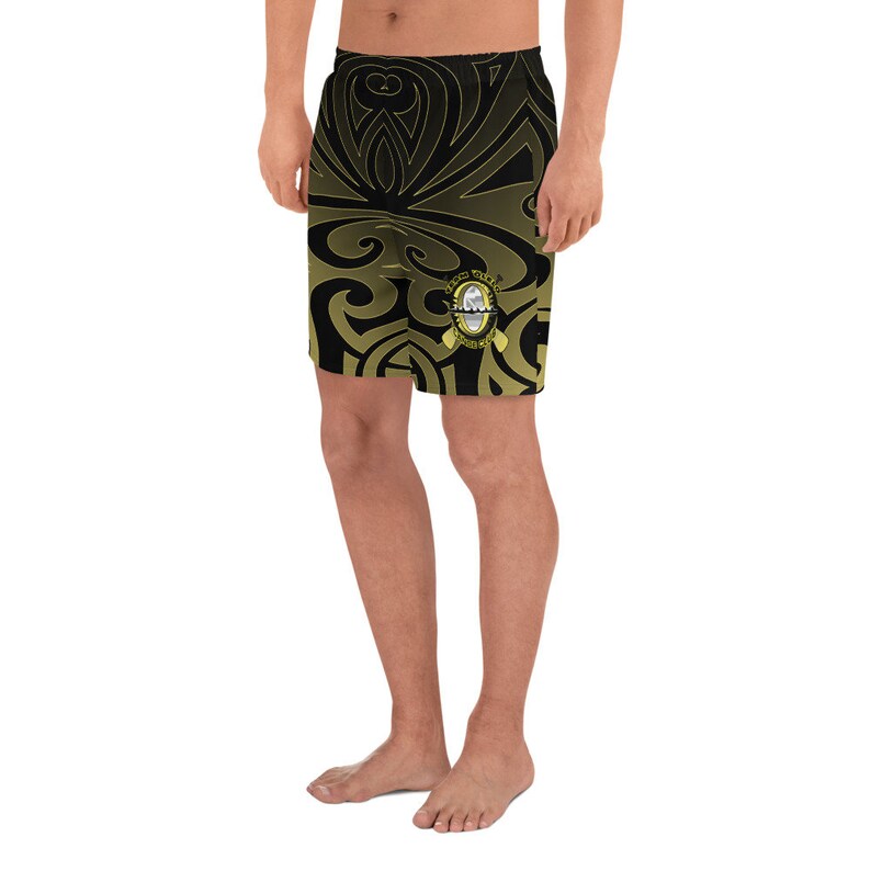 May include: Black and gold athletic shorts with a tribal design. The shorts feature a repeating pattern and a small emblem on the lower right leg. The shorts are knee-length and made of a lightweight material.