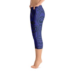 May include: Blue capri leggings with a dark blue, ornate, swirling pattern. The leggings are knee-length and form-fitting, with a high waist. The design is symmetrical and covers the entire surface of the leggings. The background is white.