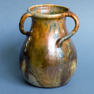 Peut inclure: Un vase en céramique brun avec deux anses. Le vase a un glaçage marbré avec des nuances de brun, de vert et de bleu.