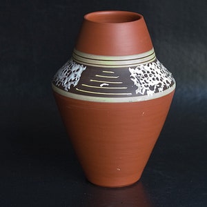 May include: A terracotta vase with a geometric design in white and brown. The vase has a wide base and a narrow neck.