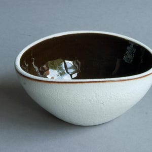 May include: A white ceramic bowl with a brown interior. The bowl has a textured exterior and a rounded shape.