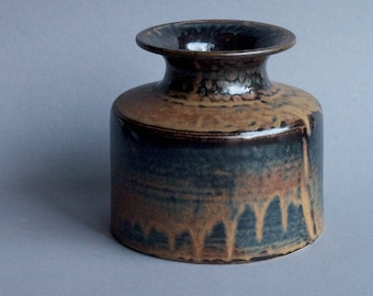 Könnte beinhalten: Eine braune und schwarze Keramikvase mit einer breiten Öffnung und einem abgerundeten Körper. Die Vase hat eine gesprenkelte Glasur mit braunen Glasurtröpfchen.
