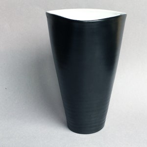 May include: A black ceramic vase with a white interior and a slightly flared opening. The vase has a smooth, glossy finish.