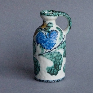 Könnte beinhalten: Ein kleiner weißer Keramik Krug mit einem grünen, blauen und gelben Blumendesign. Der Krug hat einen Henkel und einen runden Körper.
