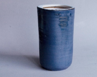 May include: A tall, cylindrical ceramic vase with a blue glaze. The vase has a slightly textured surface and a white interior.