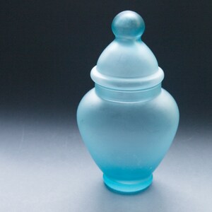Peut inclure: Un pot en verre bleu givré avec un couvercle. Le pot est rond et a une large ouverture. Le couvercle est bombé et a un bouton sur le dessus.