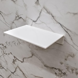 Puede incluir: Un estante rectangular blanco con una superficie lisa y plana y un soporte de montaje inclinado hacia abajo, fijado a una pared con un patrón de mármol blanco y gris con vetas oscuras prominentes en toda la superficie.
