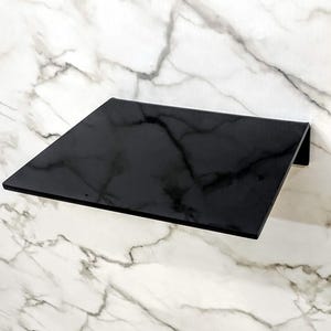 May include: A black wall-mounted shelf with a slightly angled surface. The shelf is made of a smooth, glossy material.
