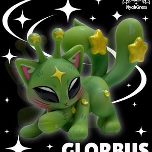 May include: A green alien cat figure with star accents. The figure has large black eyes, pink inner ears, and a yellow star on its forehead. The figure is posed on a black background with white star and swirl graphics. The word "GLORBUS" is printed in white.