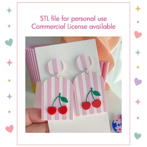 Op de afbeelding: Een paar hangende oorbellen met een roze en wit gestreept boogontwerp met een motief van rode kersen en groene blaadjes. De tekst erboven luidt: STL file for personal use, Commercial License available. De oorbellen zitten op een witte kaart.