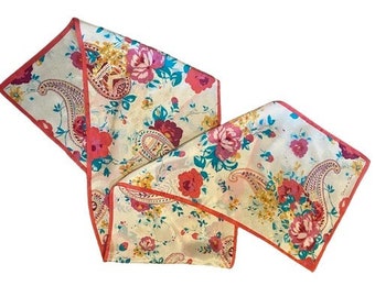 May include: A white scarf with a floral and paisley print. The scarf has a coral pink border and features pink, yellow, and blue flowers.