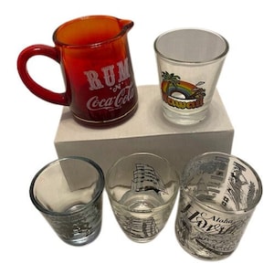 Può includere: Set di cinque bicchieri da shot in vetro con vari disegni. Un'unica caraffa di vetro rossa con la scritta "Rum 'n' Coca-Cola" stampata su di essa.