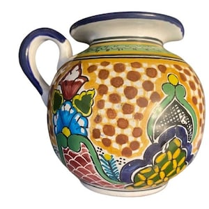 May include: A hand-painted ceramic pitcher with a yellow, orange, red, blue, green, and black floral design. The pitcher has a round body and a handle.