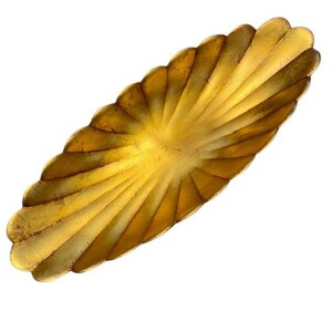 May include: A decorative, elongated gold-colored dish with a scalloped edge. The dish has a fan-like design with radiating lines, creating a textured surface. The metallic finish gives it a vintage or antique appearance. Ideal for serving or display.