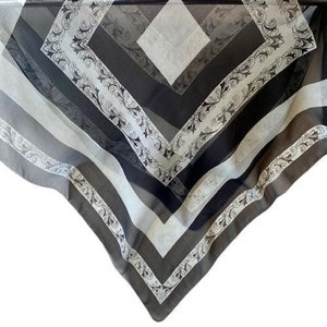 May include: A black and white patterned scarf with a geometric design. The scarf is made of a sheer fabric and has a fringed edge.