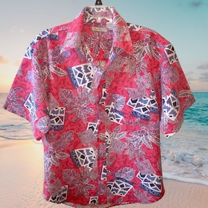 May include: A pink, blue, and white short-sleeved button-down shirt with a tropical print. The shirt has a geometric pattern with leaves and a pocket on the left side.