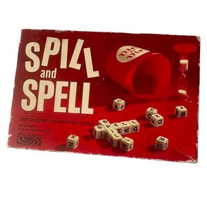 May include: A vintage "Spill and Spell" board game with a red background. The game includes a red cup, dice with letters, and the game's title in large white letters. The box reads "The 15 Cube Crossword Game."