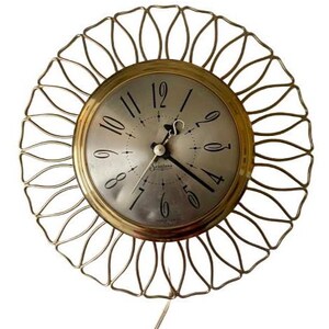 May include: A vintage wall clock with a gold-tone metal frame in a sunburst design. The clock face is silver with black numerals and hands. The clock has a cord for power.