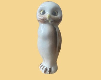 May include: A ceramic owl figurine with a white body, brown wings, and yellow eyes. The owl has a small beak and brown feet. The figurine is standing upright and has a smooth, glossy finish.