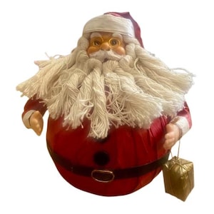 May include: A plush Santa Claus doll with a white beard and a red suit. He is wearing a white hat and has a gold belt. He is holding a small gold gift box.