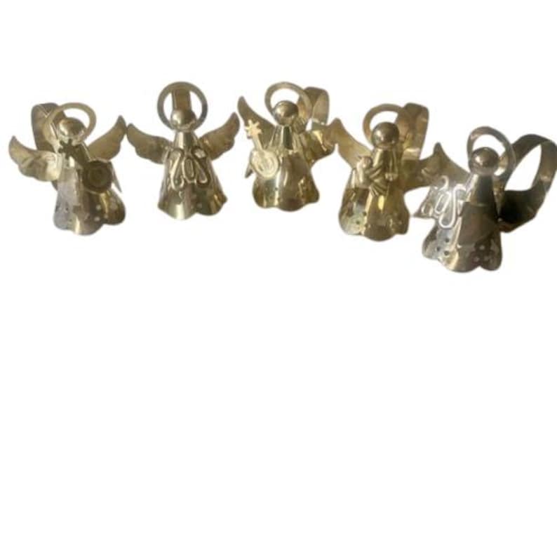 May include: Five brass angel figurines with outstretched wings. Each angel has a halo and is holding a musical instrument or object. The angels are arranged in a row against a white background.