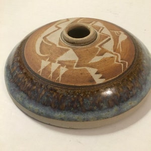 Puede incluir: Un jarrón redondo de cerámica marrón con un diseño geométrico blanco. El jarrón tiene un esmalte azul y marrón en la parte inferior.