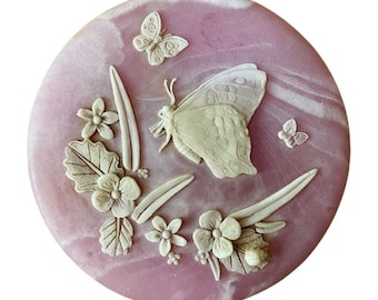 May include: A pink round trinket box with a carved design of butterflies and flowers. The box is made of alabaster.