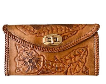 Puede incluir: Un bolso de mano de cuero marrón con un diseño floral en relieve y un cierre dorado.