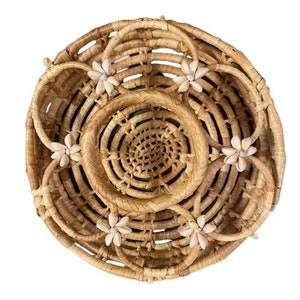 Könnte beinhalten: Ein runder geflochtener Korb in natürlicher brauner Farbe. Der Korb hat ein dekoratives Design mit weißen Muscheln am Rand.