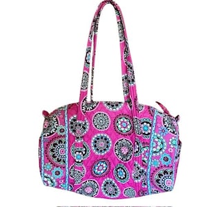 Puede incluir: Una bolsa de viaje acolchada de color rosa con un estampado floral. La bolsa tiene dos asas superiores y un cierre de cremallera.