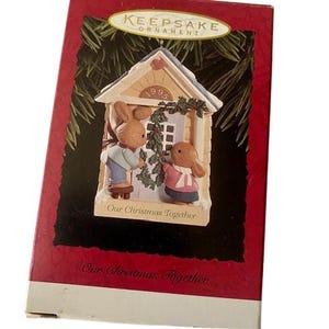 May include: A Christmas ornament depicting two rabbit figures outside a house. The ornament is in a box with the text "Keepsake Ornament" and "Our Christmas Together". The house has the year "1995" on it.