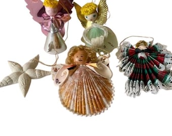 May include: A collection of Christmas ornaments featuring angel figures and a starfish. The angels have various designs, including shell-based bodies, metallic wings, and fabric skirts. The ornaments are in shades of gold, pink, green, and red, with white accents.