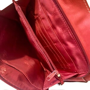 May include: Red leather wallet with multiple card slots and a zipper closure. The wallet is open to reveal the interior lining.