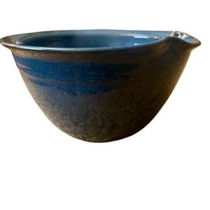May include: A handmade ceramic bowl with a dark blue exterior and a lighter blue interior. The bowl has a textured surface and a spout on one side. The bowl is ideal for serving or as a decorative piece.