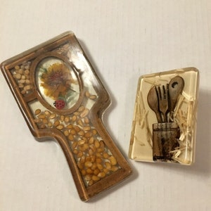 May include: Two resin pot holders with a wood frame. One features a yellow flower with a ladybug and the other has a set of wooden kitchen utensils in a jar.