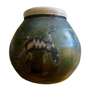 May include: A ceramic jar with a rounded body and a light-colored rim. The jar is primarily green with a dinosaur illustration in black and white. The dinosaur is depicted in a stylized, artistic manner.