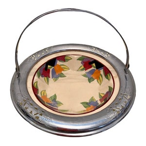Puede incluir: Un plato de servir vintage plateado con un asa. El plato tiene un cuenco de cerámica blanca con un diseño floral en tonos rojos, naranjas, amarillos, azules y verdes.