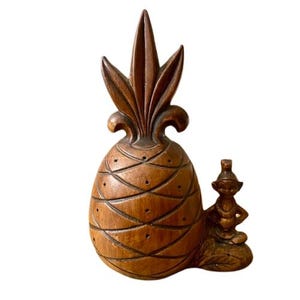 Könnte beinhalten: Eine Ananas-Figur aus Holz mit einem geschnitzten Design und einer kleinen Holz-Tiki-Figur, die daneben sitzt.