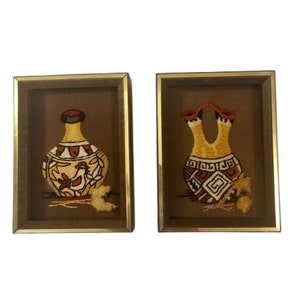 Puede incluir: Dos imágenes bordadas enmarcadas de cerámica nativa americana. La cerámica es en tonos de marrón, naranja y amarillo. Los marcos son dorados.