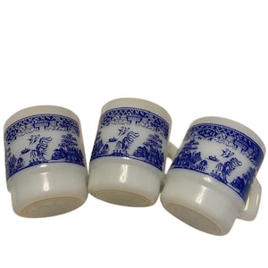 Puede incluir: Tres tazas de cerámica blanca con diseños de sauce azul y blanco. Las tazas son todas del mismo tamaño y forma.