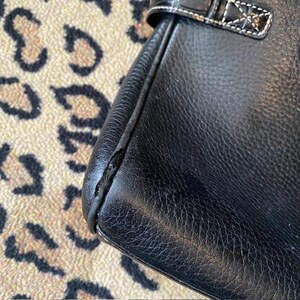 K&ouml;nnte beinhalten: Nahaufnahme einer schwarzen Ledertasche mit wei&szlig;en N&auml;hten. Die Tasche hat eine glatte, strukturierte Oberfl&auml;che.