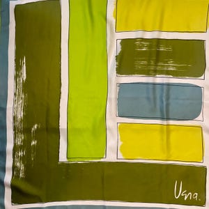 May include: A square scarf featuring a geometric pattern of rectangular blocks in olive green, lime green, and muted blue on a white background. The design includes thick brushstroke textures and black outlines. The word "Una." is printed in white in the corner.
