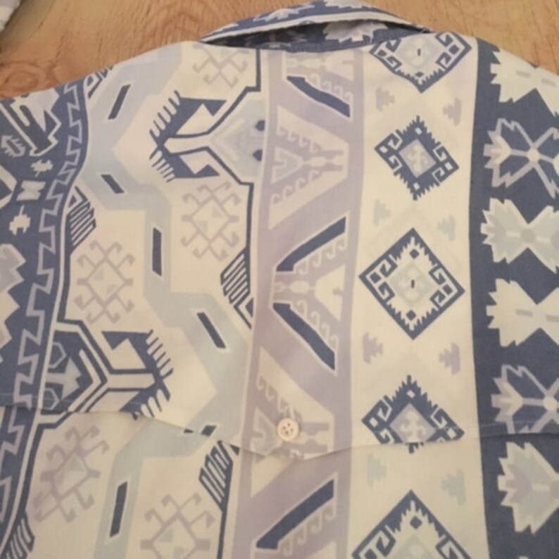 May include: A white and blue patterned shirt with a geometric design. The shirt has a button-up collar and a single button on the front.