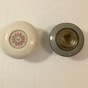 Może przedstawiać: Dwa ceramiczne pojemniki z pokrywką. Jeden jest biały z różowym i zielonym wzorem kwiatowym na pokrywce. Drugi to jasnoniebieski i brązowy pojemnik.